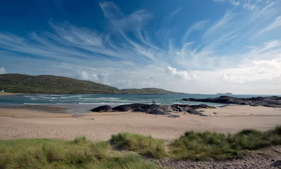 Derrynane Beach on southwest corner of the Ring of Kerry. County Kerry, Ireland. Sweeping blue sky with two figures standing on a rock.