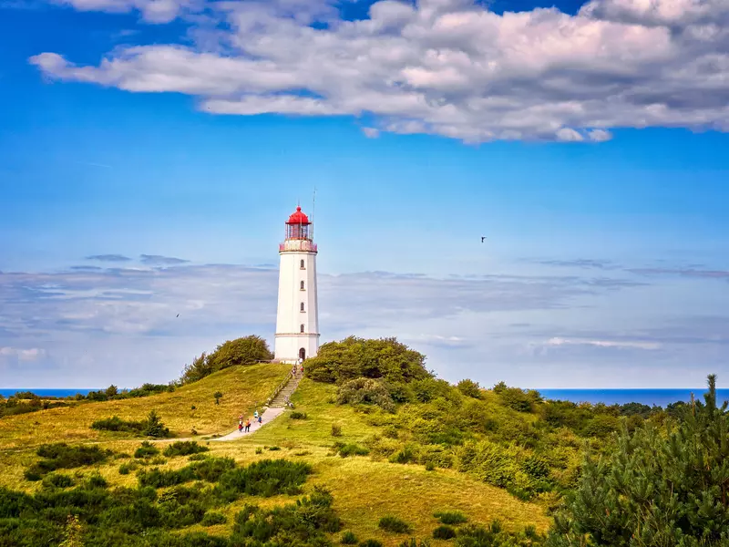 A lighthouse on a grassy hill overlooking a waterway on a bright, sunny day.