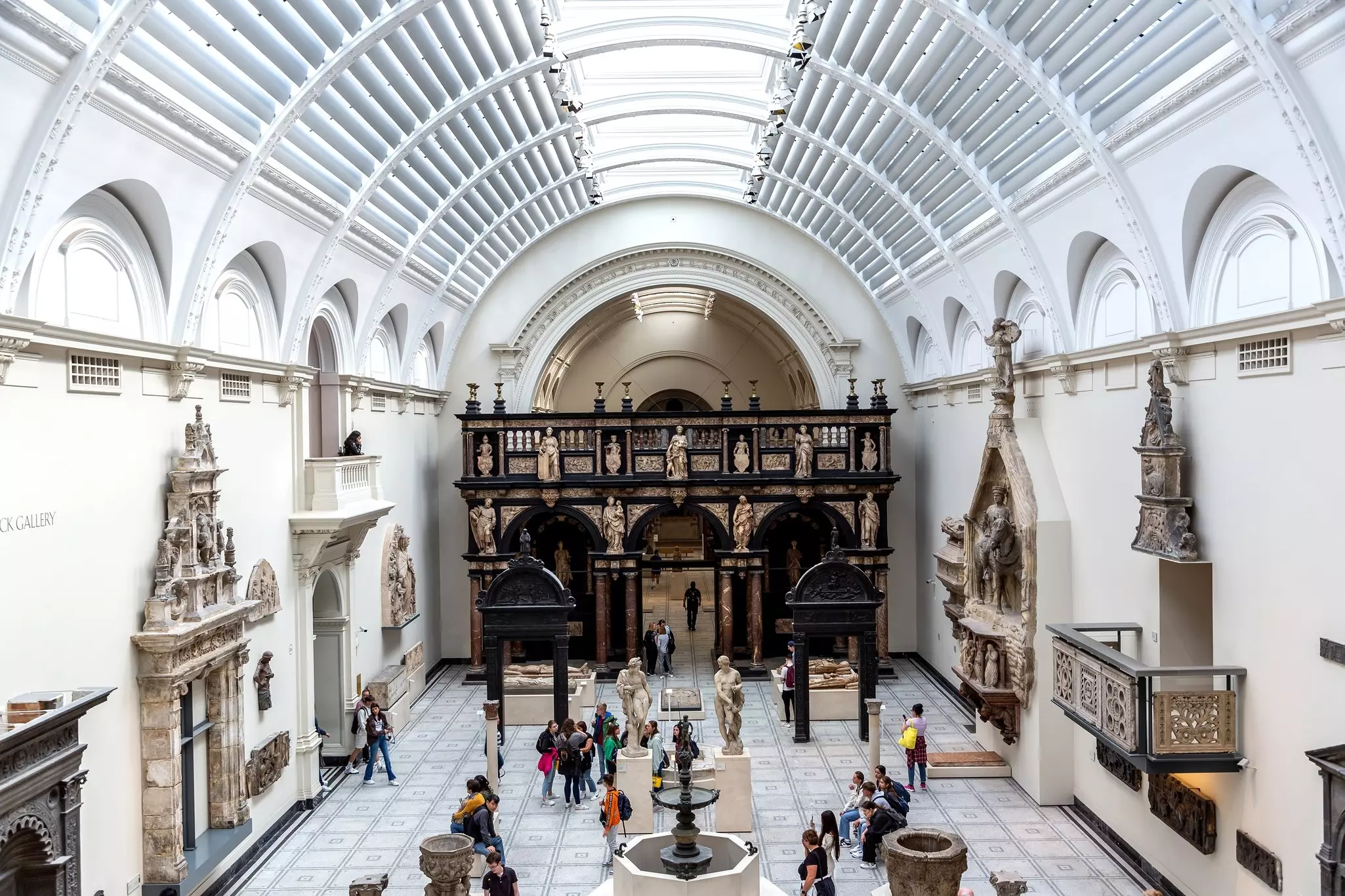 Visitors and tourists look around a large gallery full of ornate Renaissance sculptures and carvings.