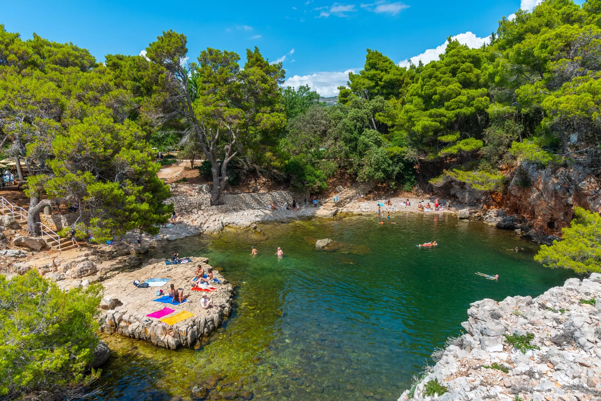 People swimming and sunbathing at a sheltered bay on a forested island.