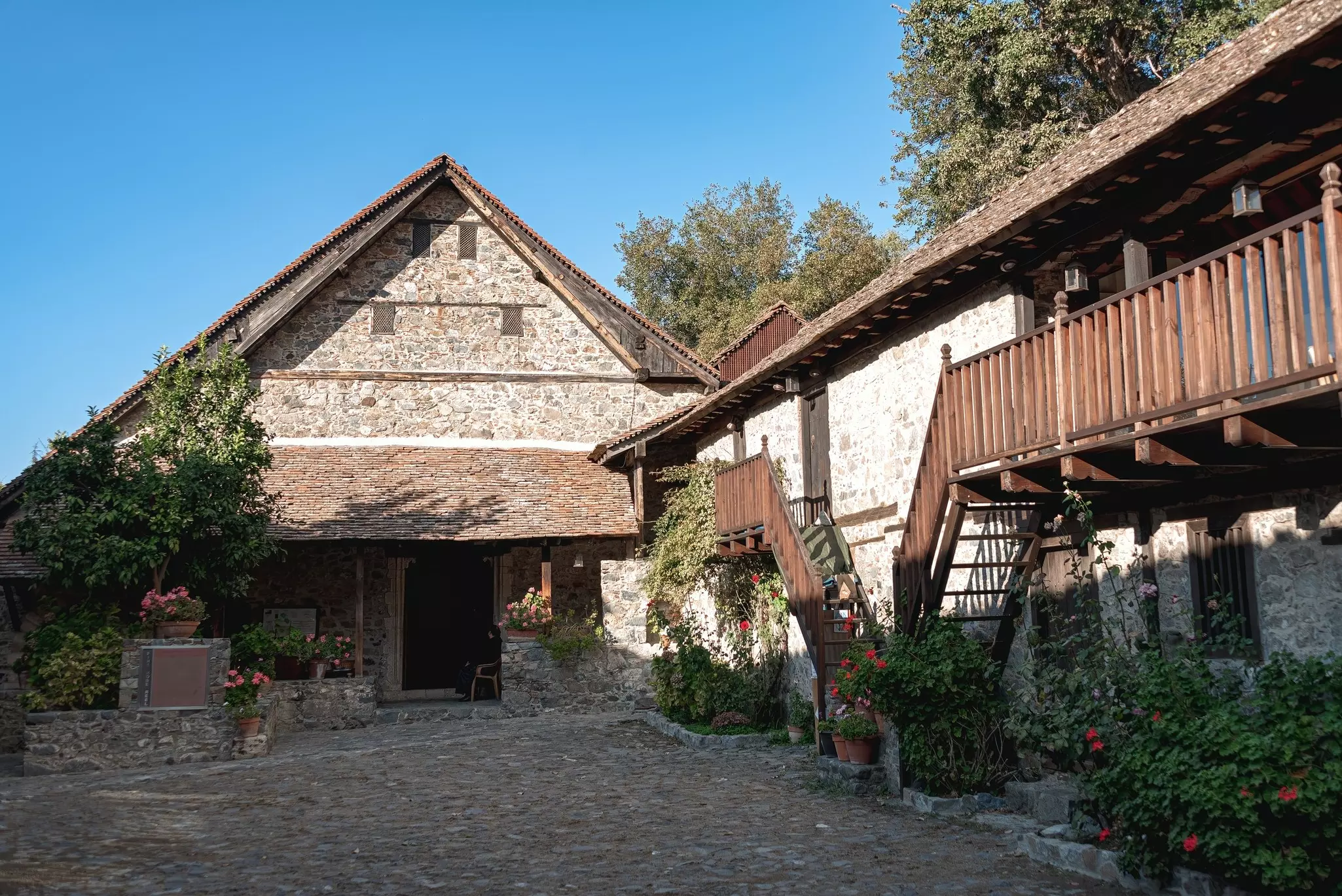 A rustic stone building with a wooden roof in a cobbled courtyard.