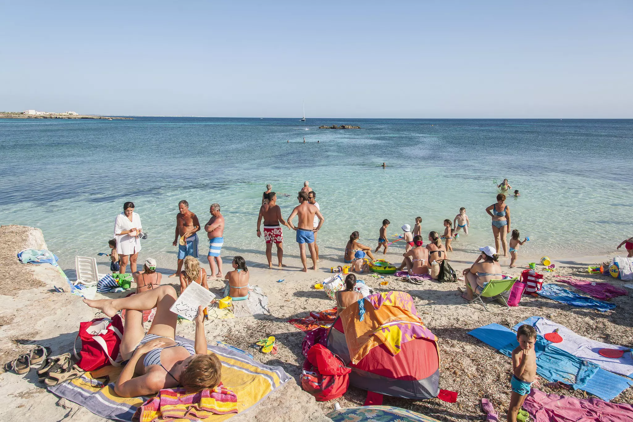 Busy shot with people relaxing on the rocks after a dip in the clear blue water at Cala Rossa, Favignana
