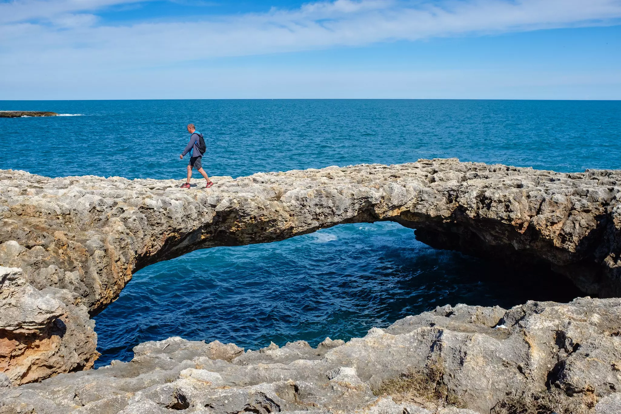 A person crosses a natural rock bridge in Italy over the sea.