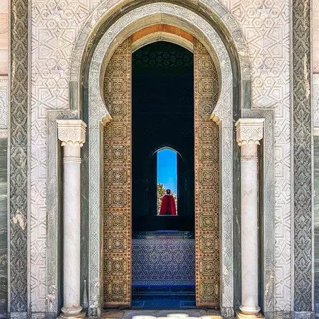 A doorway with carvings and columns leads to a dark passageway; a person is in the doorway at the other end.