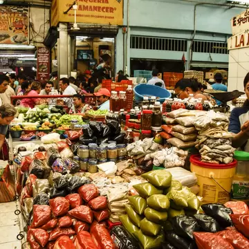 Market stall stacked with bagged spices and chillies, with shoppers and vendors in a busy covered hall.