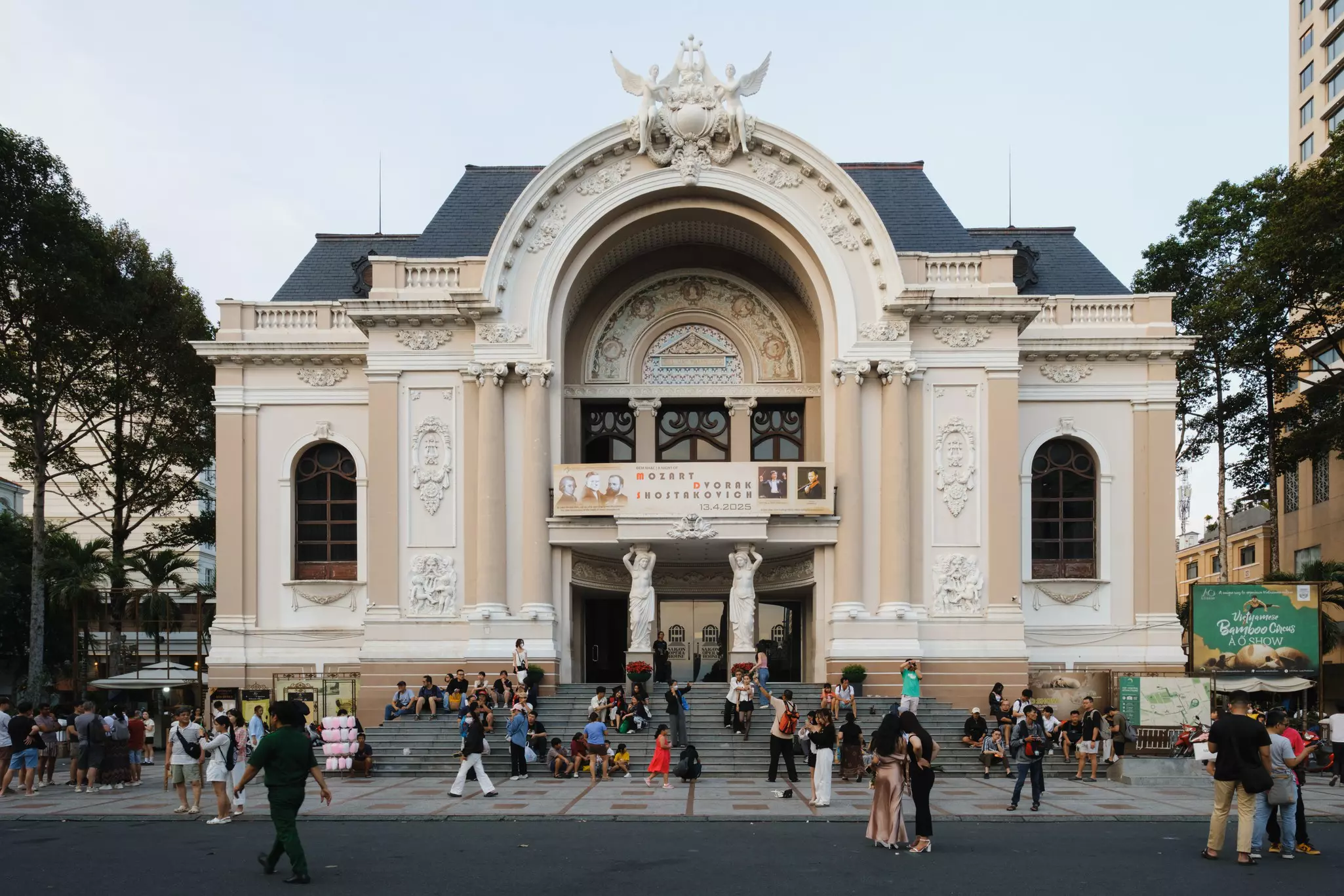 People walking near and sitting on the steps of the Saigon Opera House in Ho Chi Minh City