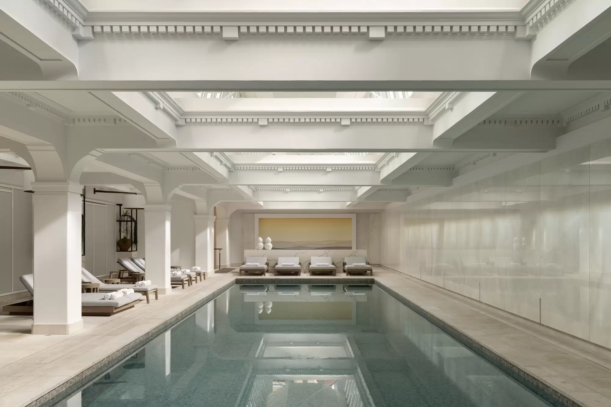 An indoor pool surrounded by white chaises and white walls