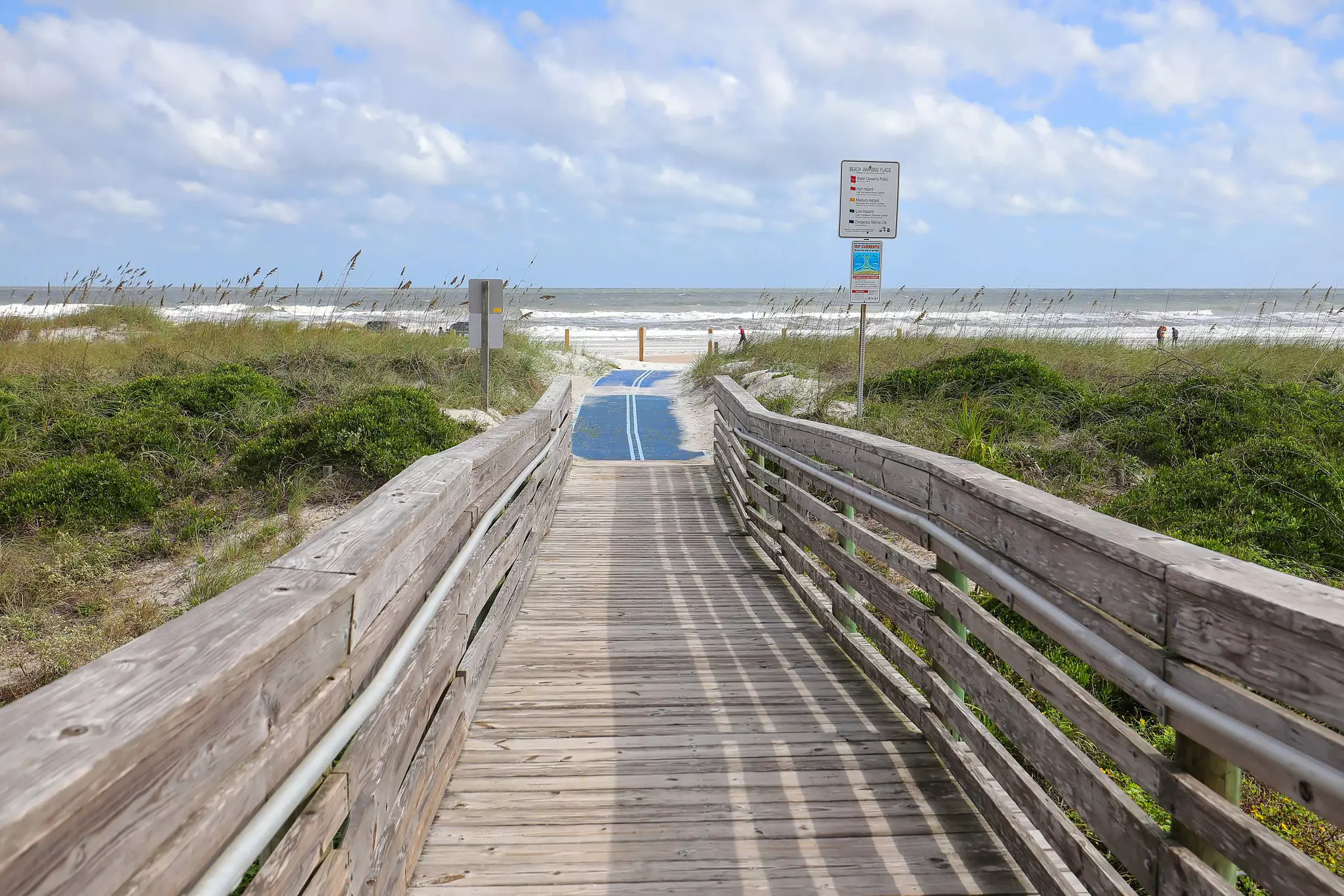 A blue mat at the end of a wooden ramp extends access to a beach for people in wheelchairs