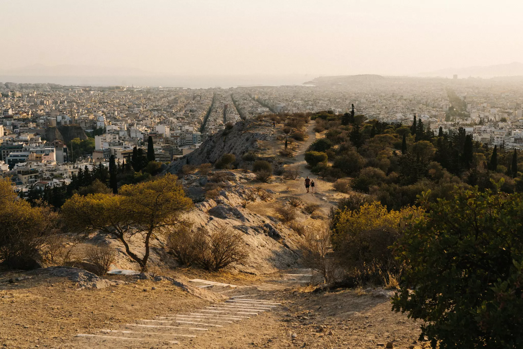 A walkway along a dusty hillside overlooking a spread-out city in the distance.