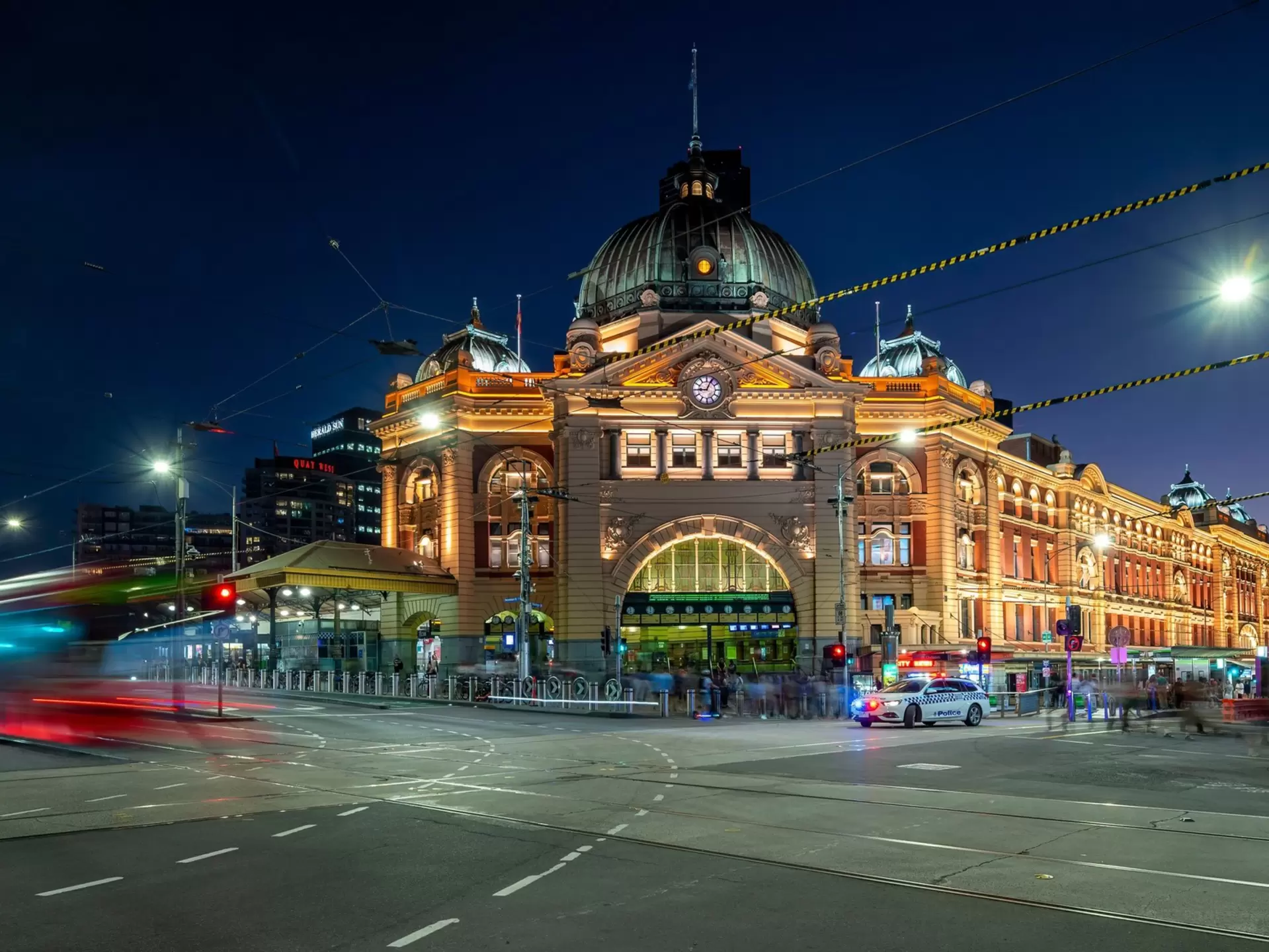 Flinders St station by night, with passing trams and traffic creating light trails motion blur