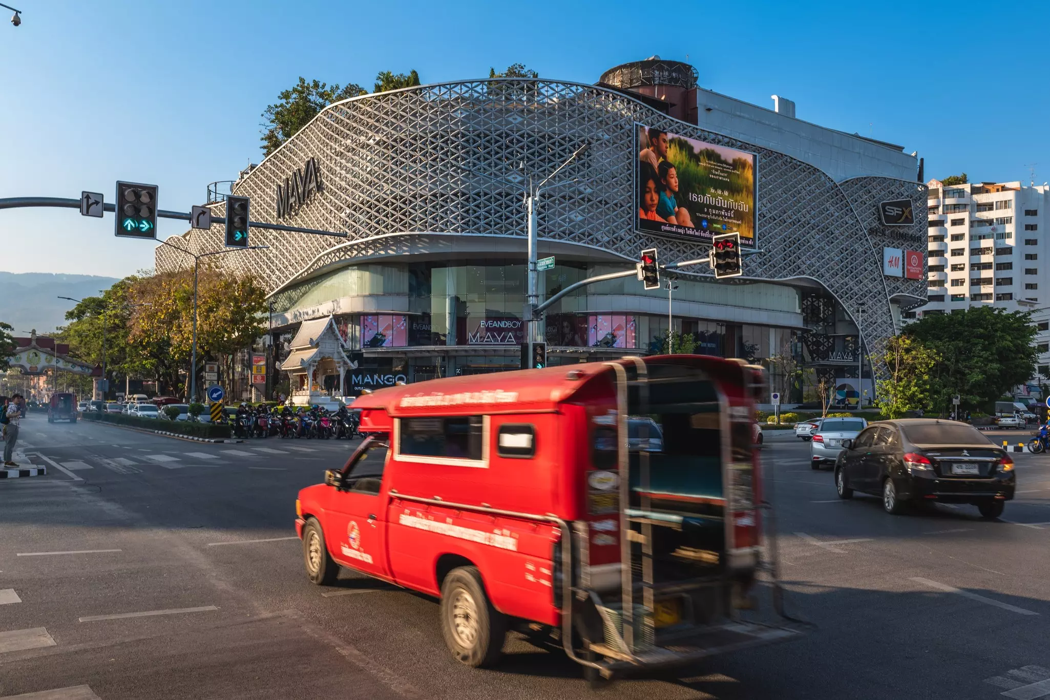 A red truck passes by a large shopping center on a busy city street 