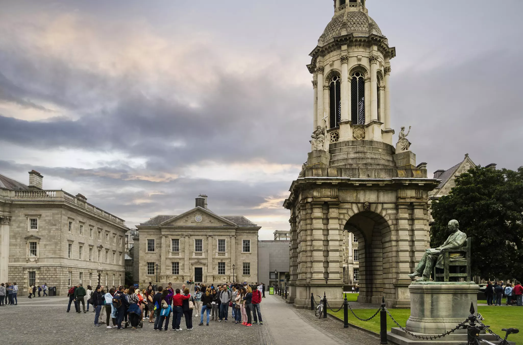 A group of people stand in a public square surrounded by historic buildings and a bronze sculpture.