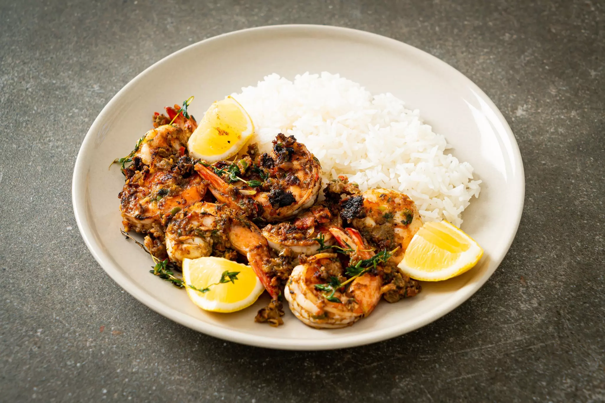 Closeup of a plate with jerk shrimp next to lemon wedges and white race.