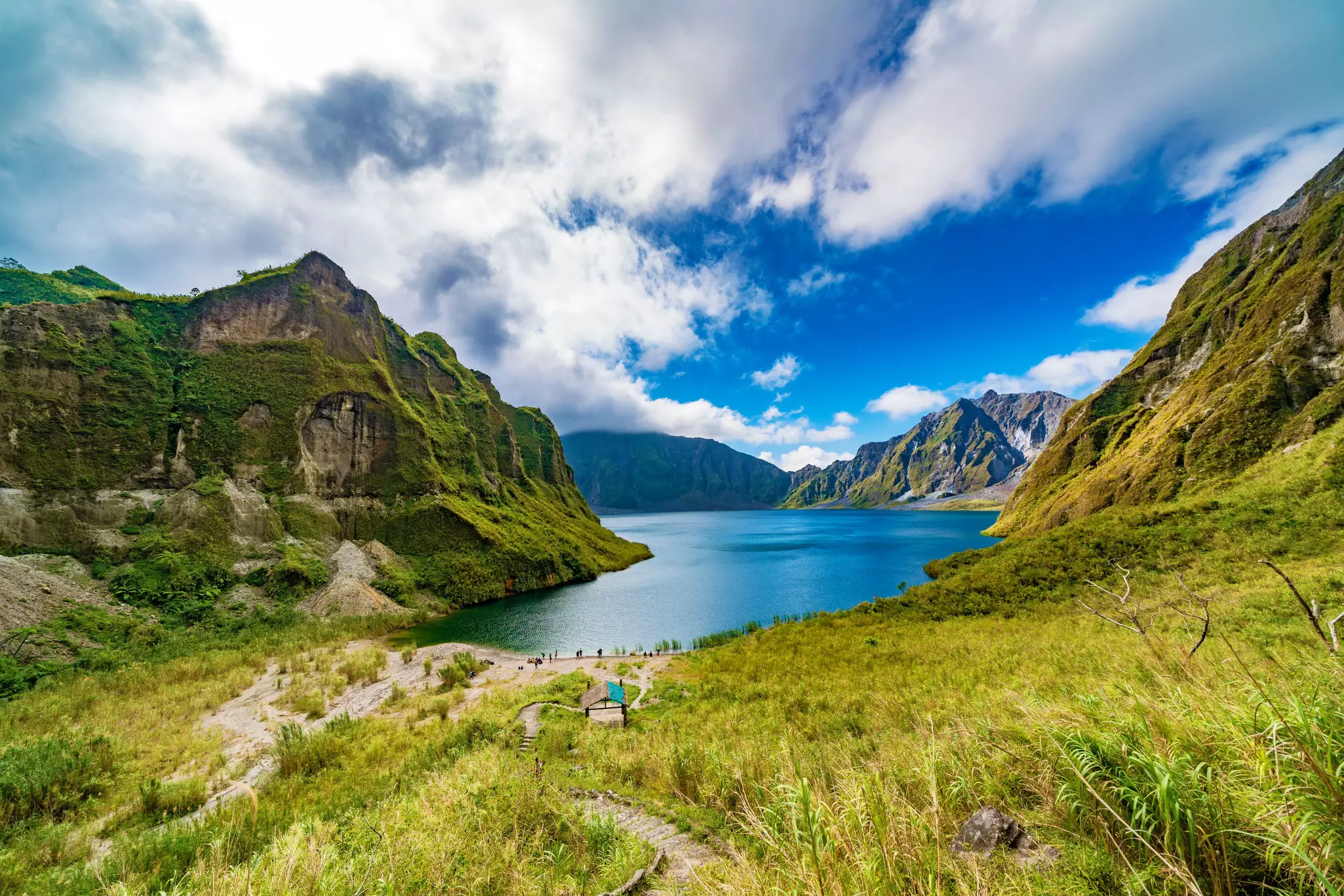 A footpath through a volcanic mountain valley leading to a central lake.