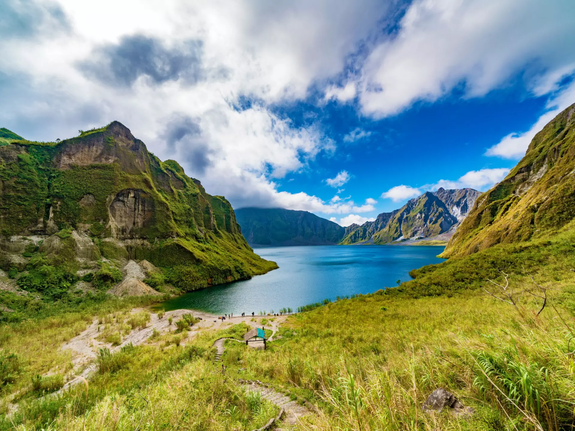 A footpath through a volcanic mountain valley leading to a central lake.