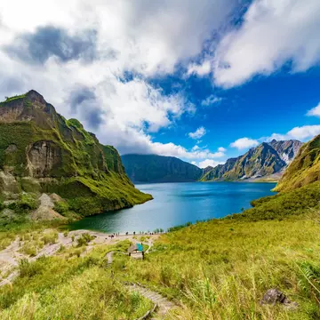 A footpath through a volcanic mountain valley leading to a central lake.