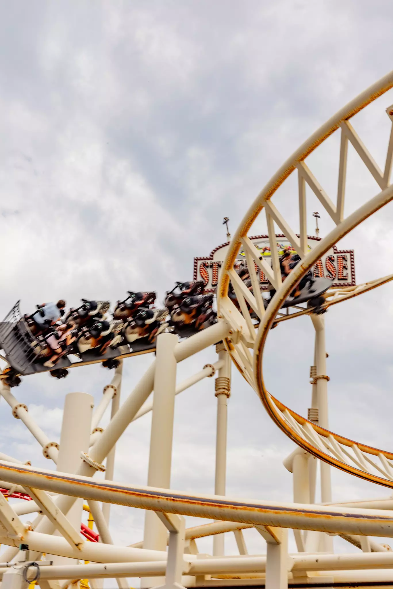 Roller-coaster cars with people round a corner on a white structure.