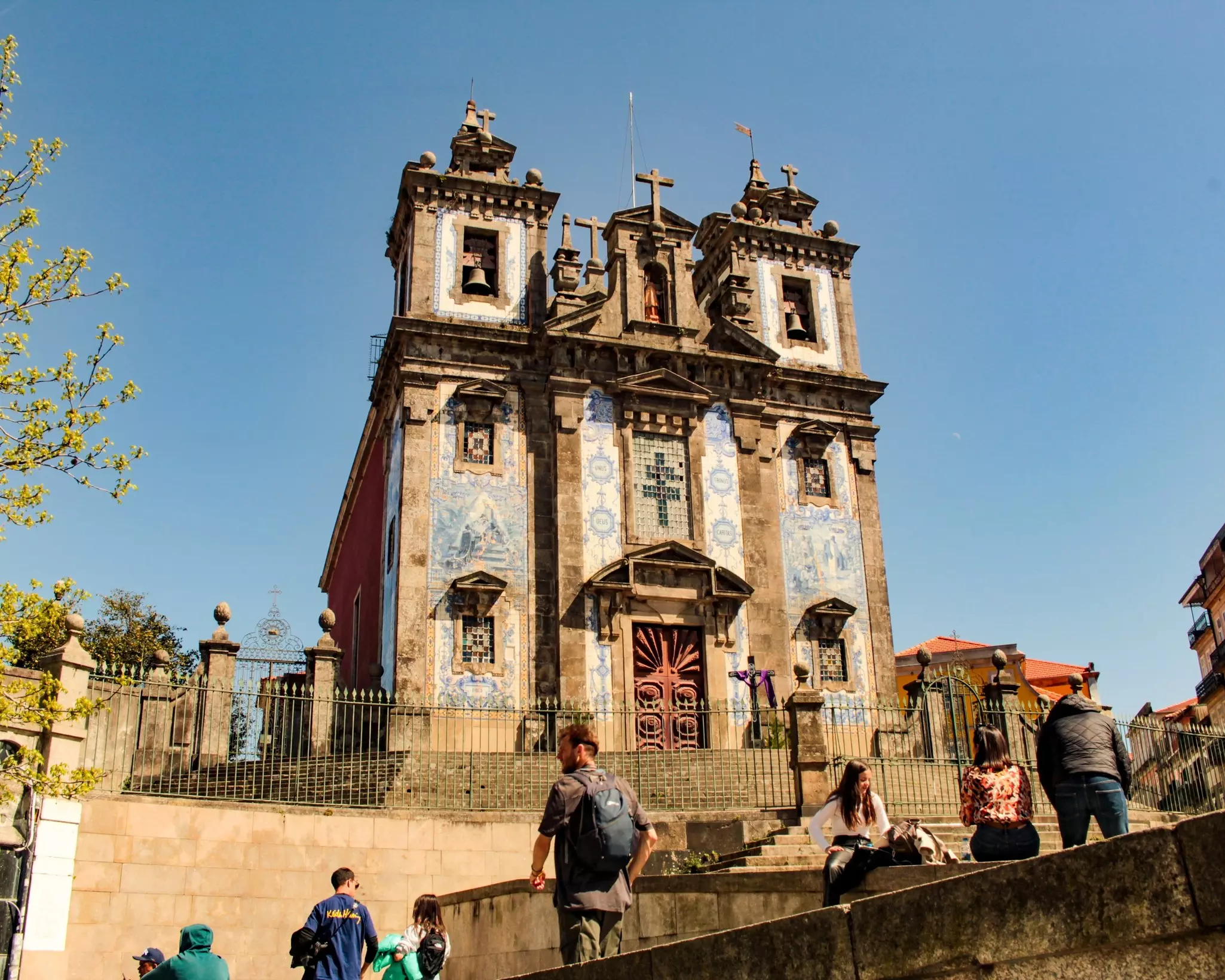 People on stone stairs leading to a church with blue-and-white tiles on the facade.
