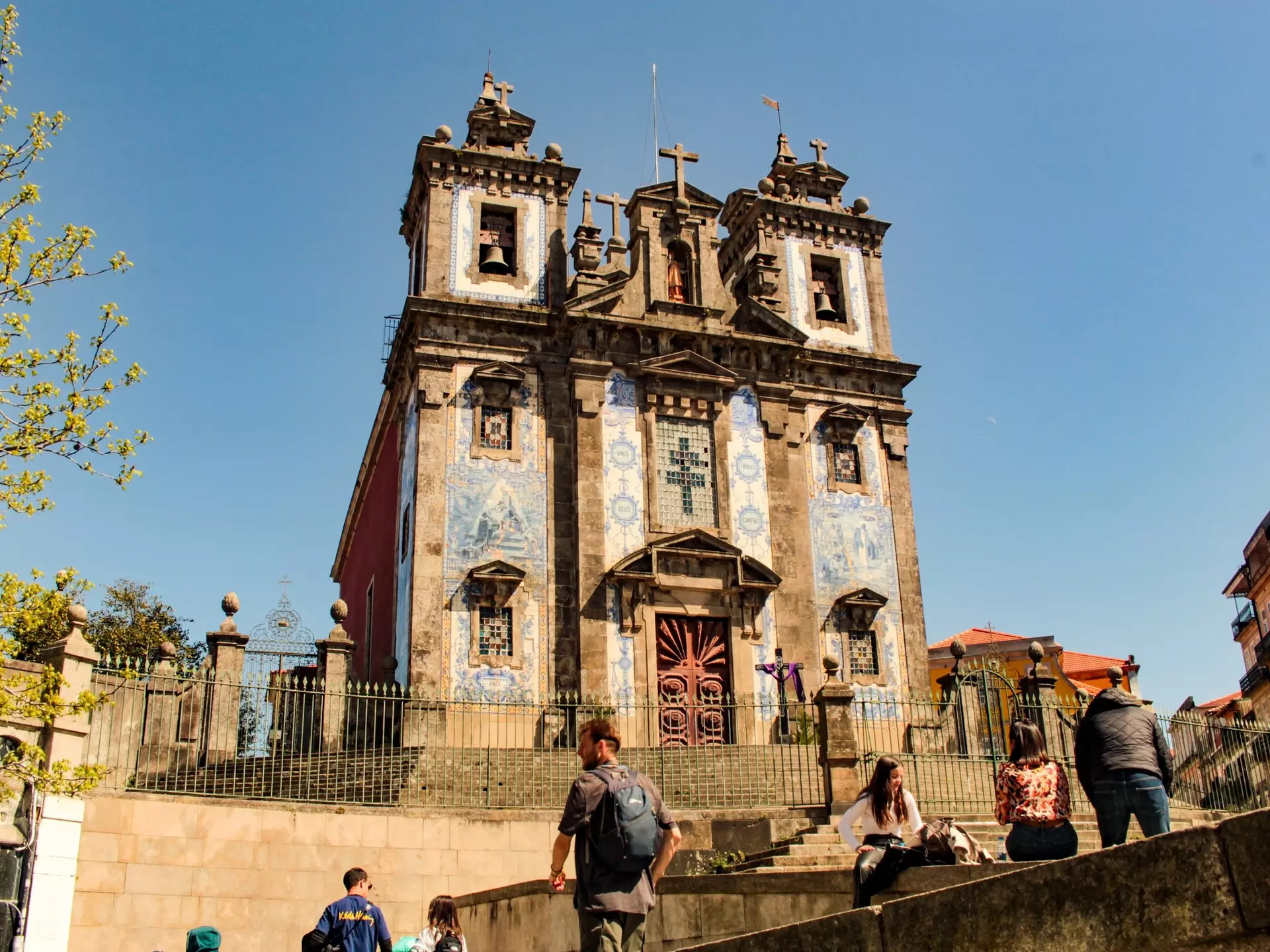 People on stone stairs leading to a church with blue-and-white tiles on the facade.