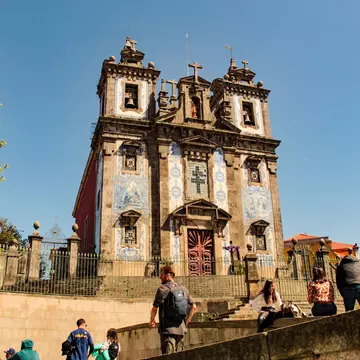 People on stone stairs leading to a church with blue-and-white tiles on the facade.