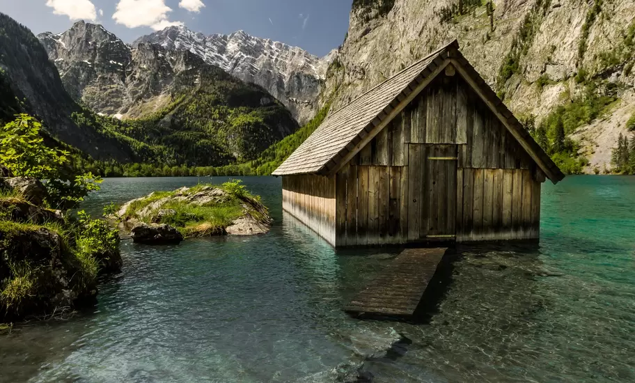 Weathered wooden boathouse standing in turquoise water on the Obersee near Berchtesgaden, beneath steep grey limestone peaks