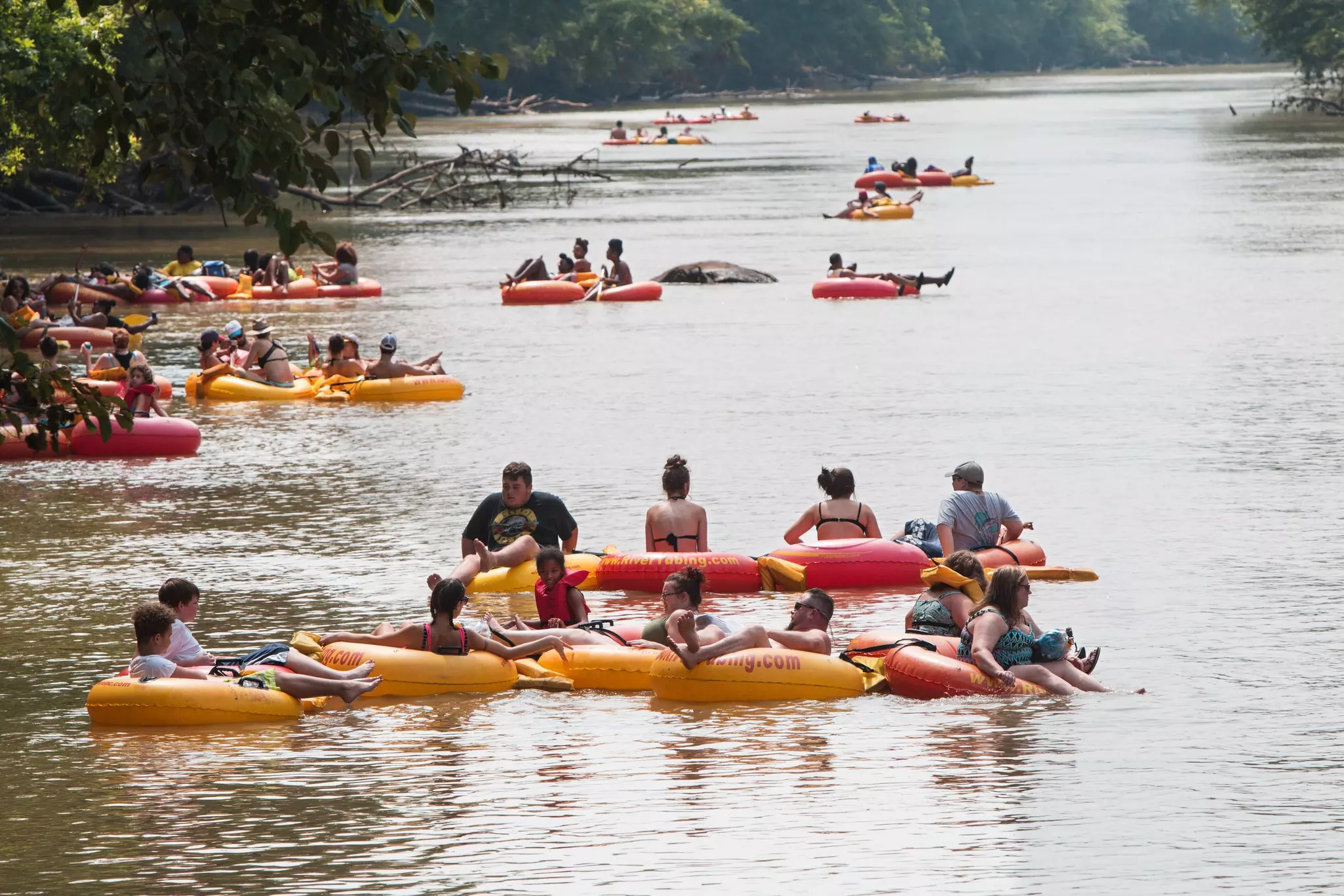 Several groups of people float down a river on rafts and inner tubes.