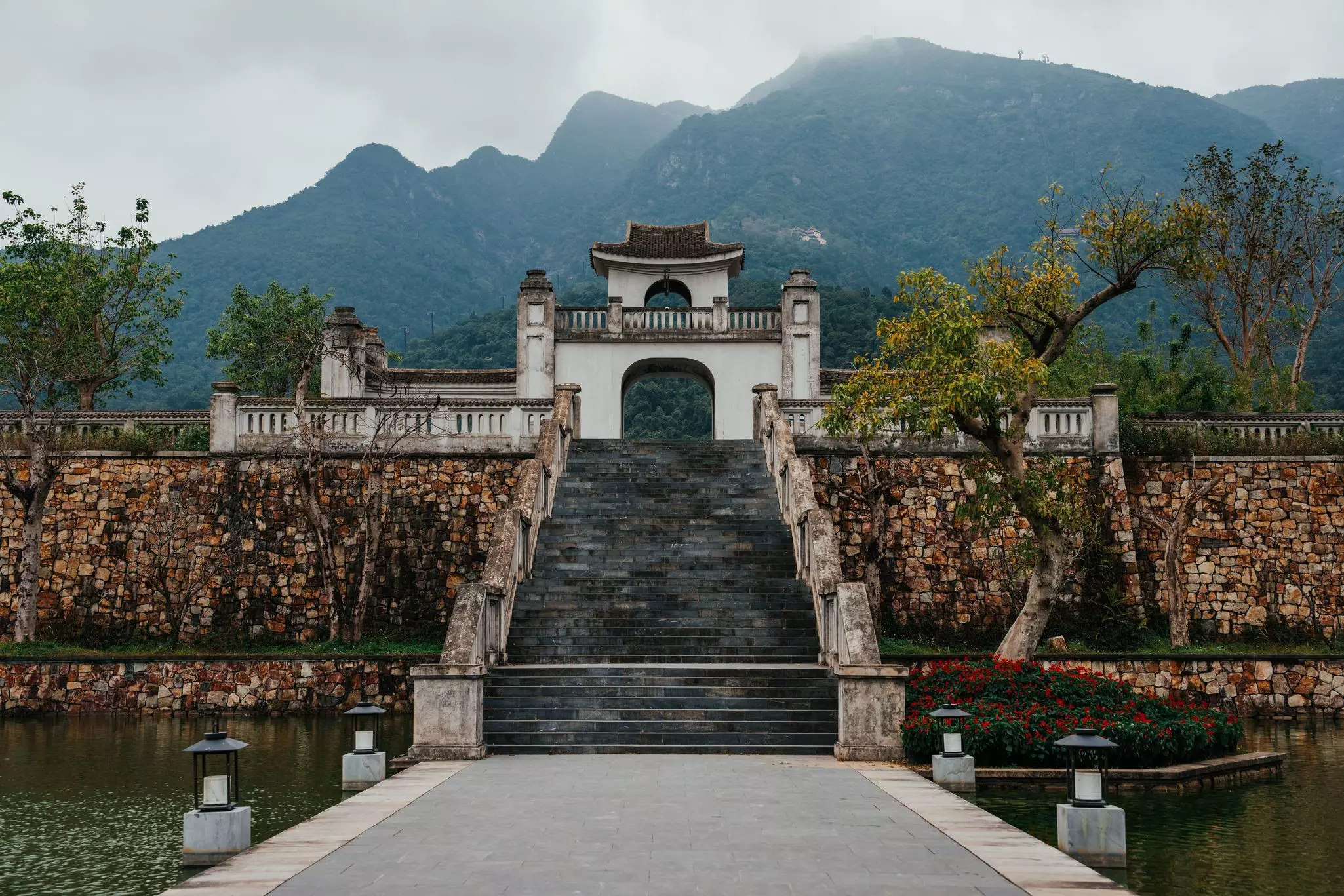 A walkway over water leads to stairs that go up to a white gate with a mountain behind it.