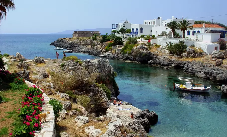 Rocky cove with turquoise water and a moored fishing boat at Avlemonas, Kythira, Greece, below whitewashed houses and a fort