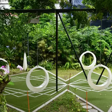 White ring-shaped swings hanging from black frames over patterned green turf among tropical plants in a Malé park