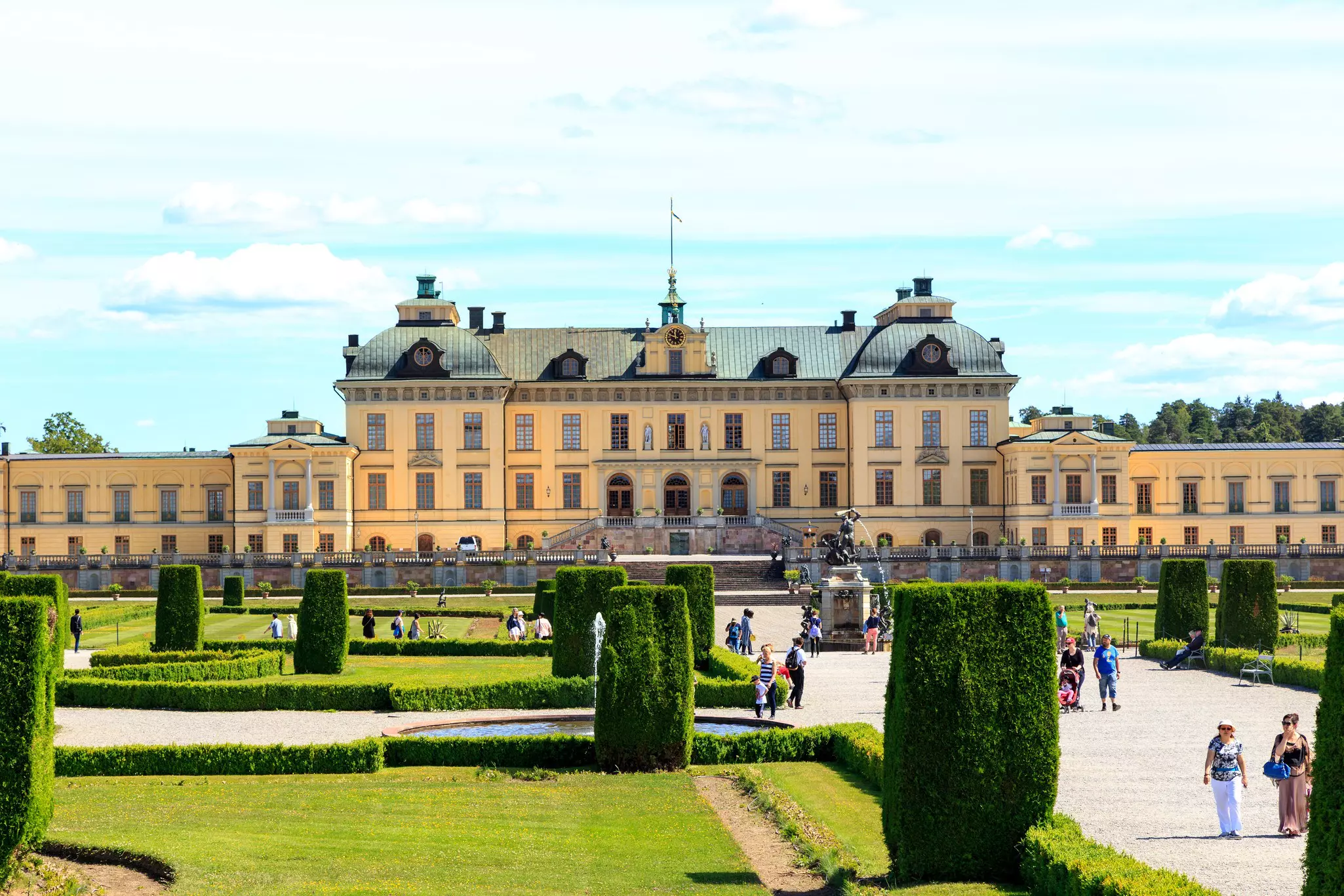 A large baroque castle in landscaped grounds. Tourists are exploring on day visits.