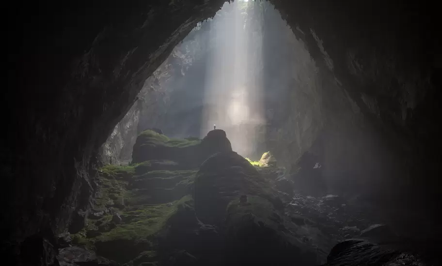 A caver stands under a beam of sunlight passing through a doline, into the world's biggest cave, Hang Son Doong.