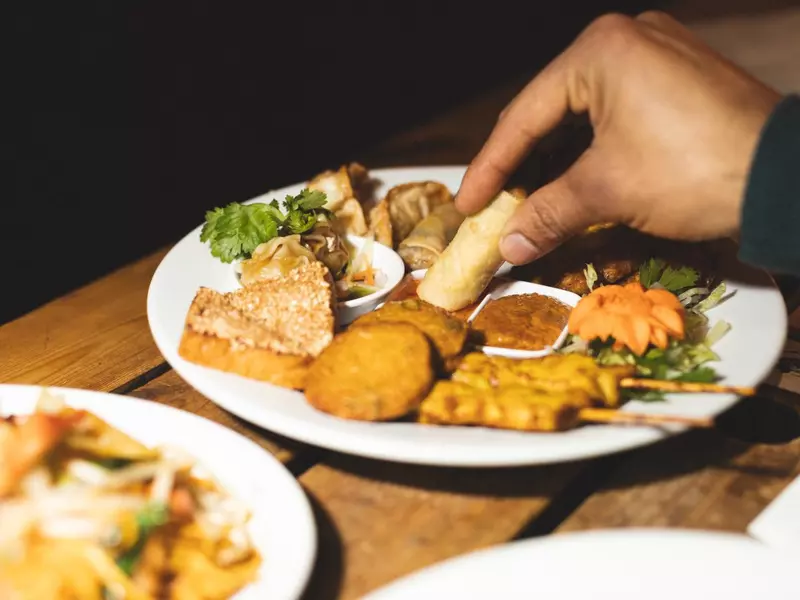 A hand reaches out for a spring roll on a plate of Thai appetizers.