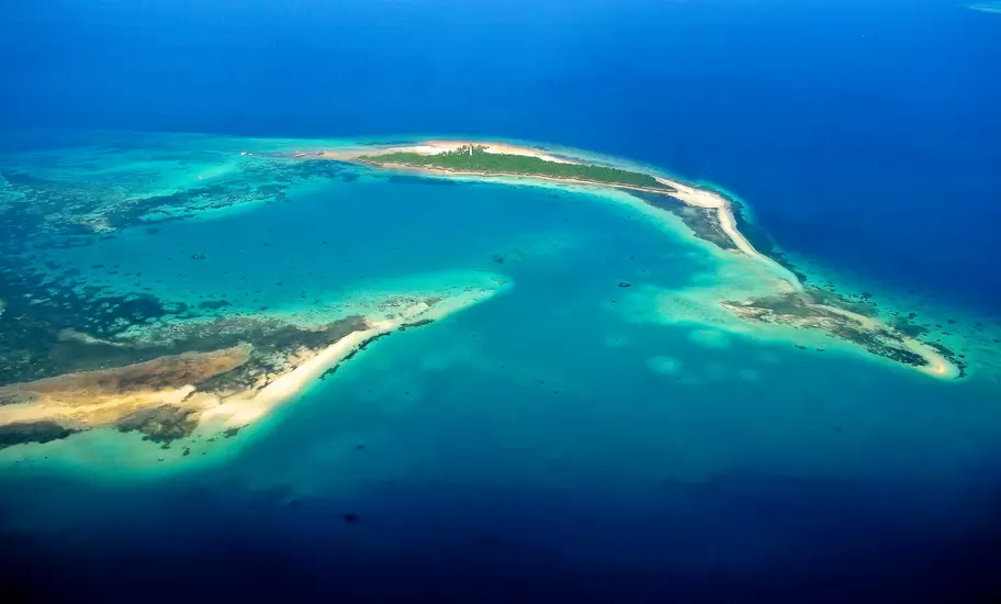 Small forested islet with a lighthouse, ringed by white sandbars and turquoise reef, seen from the air, Zanzibar Archipelago
