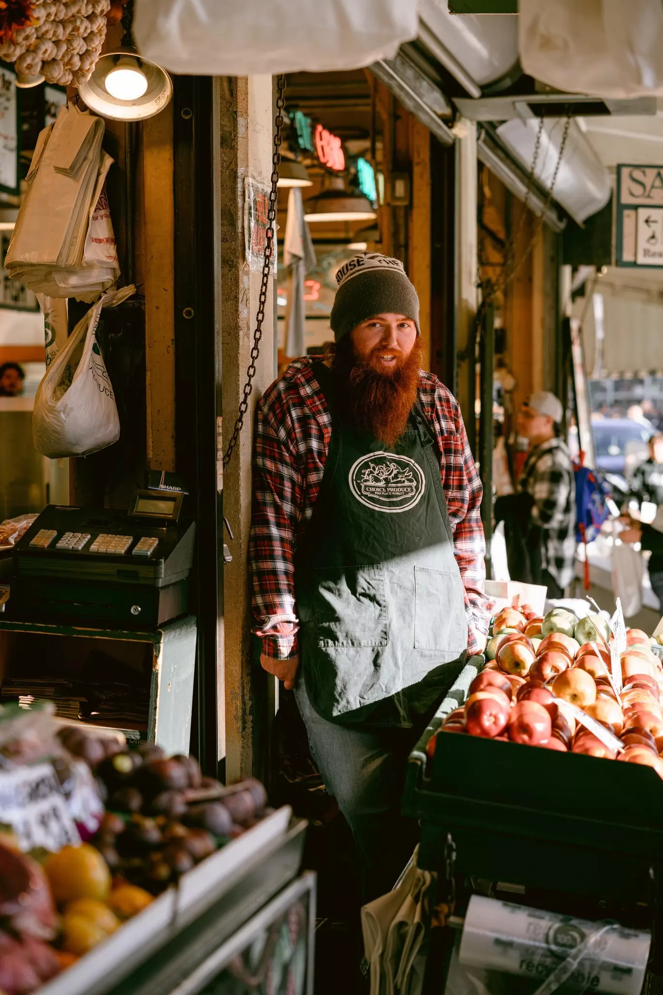  A vendor with a long red beard stands behind a fresh fruit stand