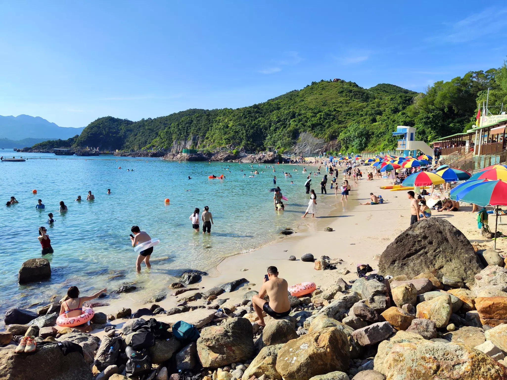 A busy beach on a sunny day with people playing on the sand and in the ocean.