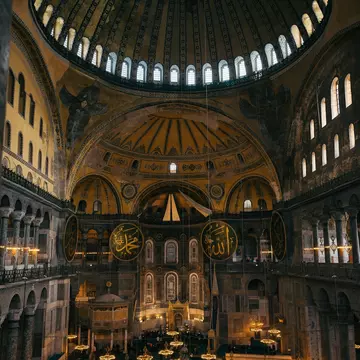 Ribbed dome on a ring of windows above seraph mosaics, gold calligraphic roundels and low chandeliers over green carpet.