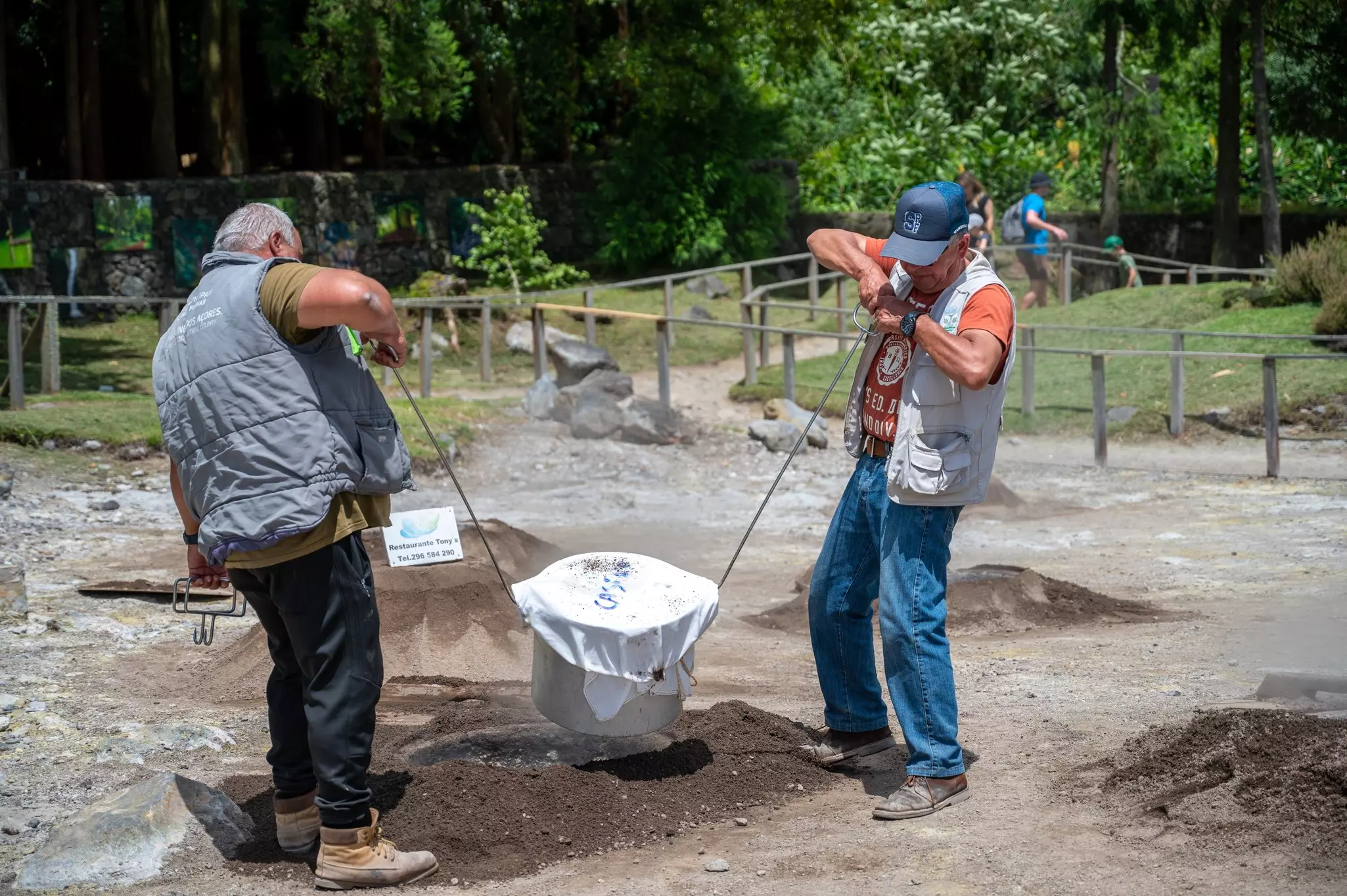 Two men remove a pot covered in cloth from the ground.