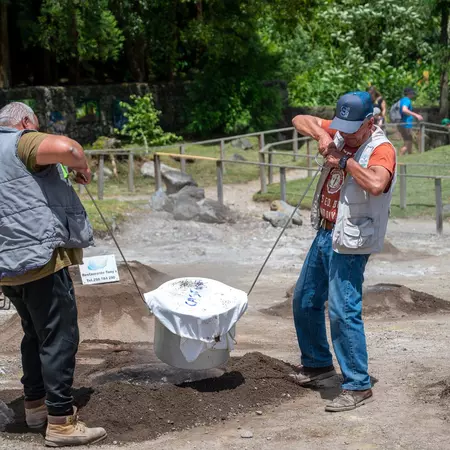Two men remove a pot from the ground that has been cooked by the heat of volcanic activity.