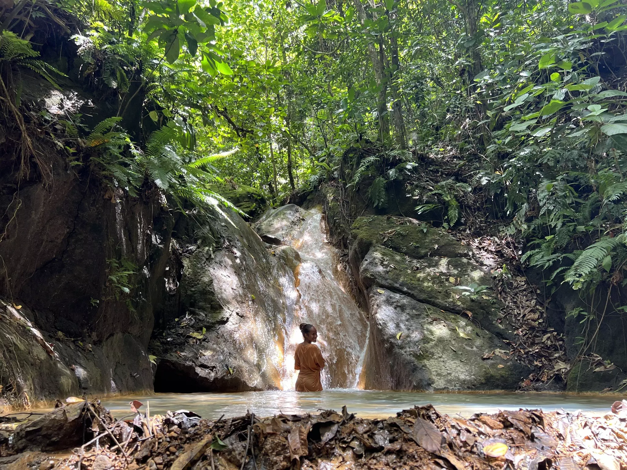 A woman bathes in a hot spring with a small waterfall in jungle