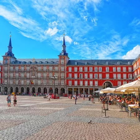 Tourists walk on the cobblestones and sit outside in cafes at Plaza Mayor, Madrid