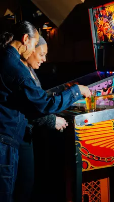 Two women playing at a pinball  machine