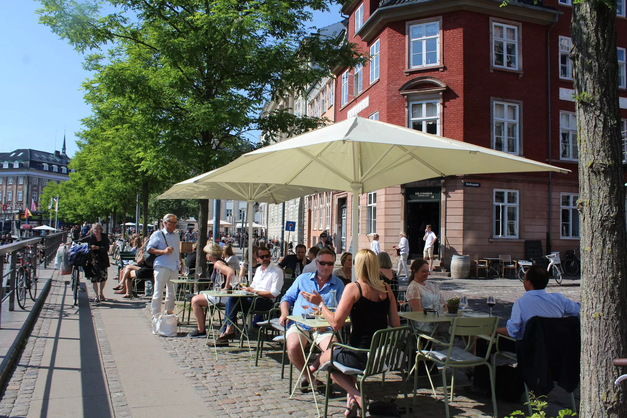 People sit in the sun at an outdoor cafe with umbrellas.