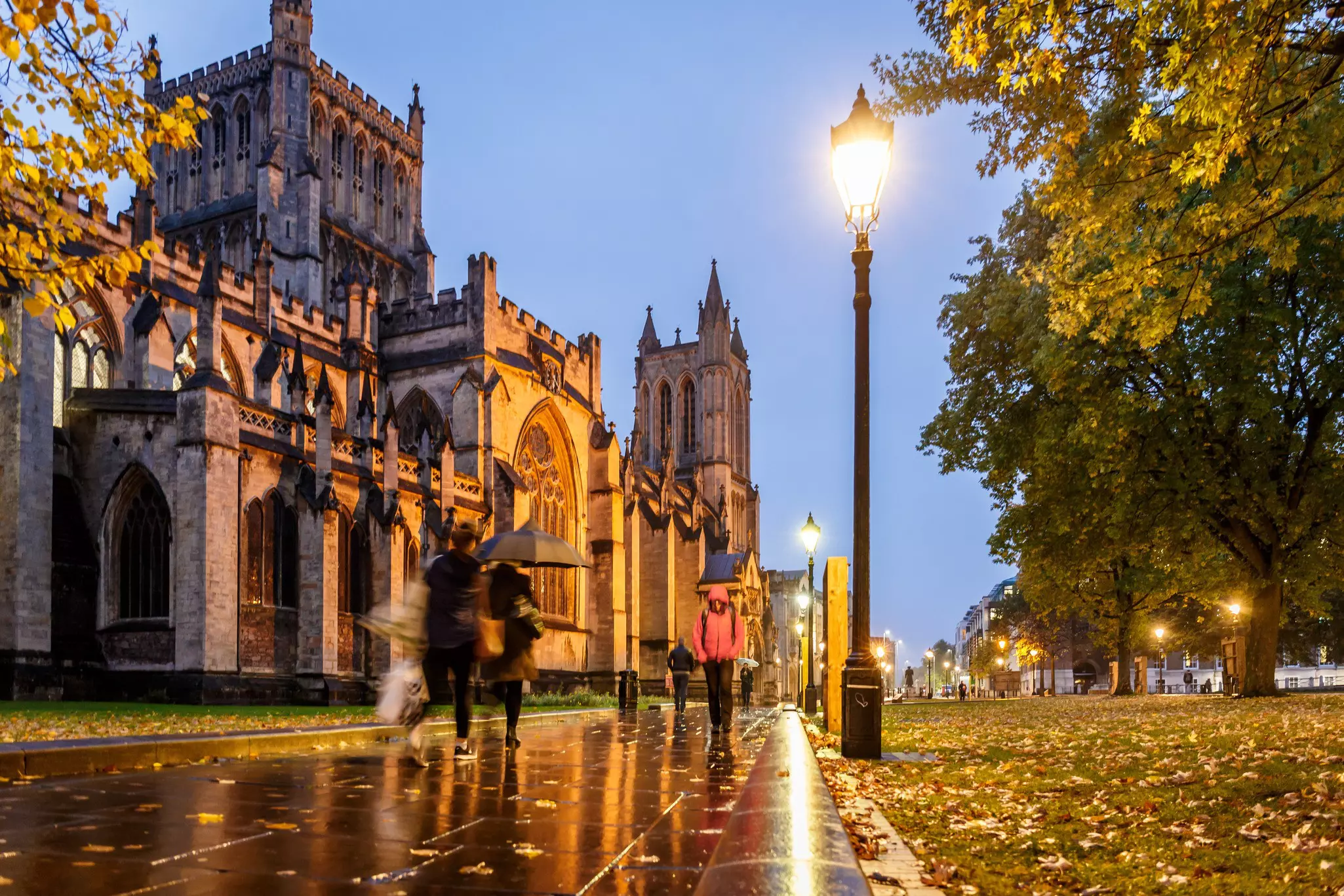 People in coats hurry through the rain on a city street on an autumn evening.