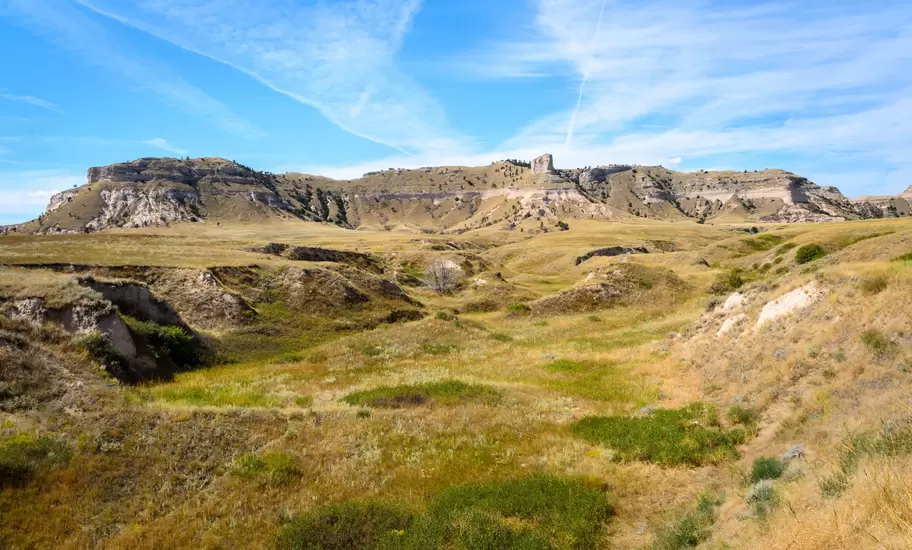 Sandstone bluffs of Scotts Bluff rise above rolling prairie and eroded gullies in western Nebraska under a pale blue sky