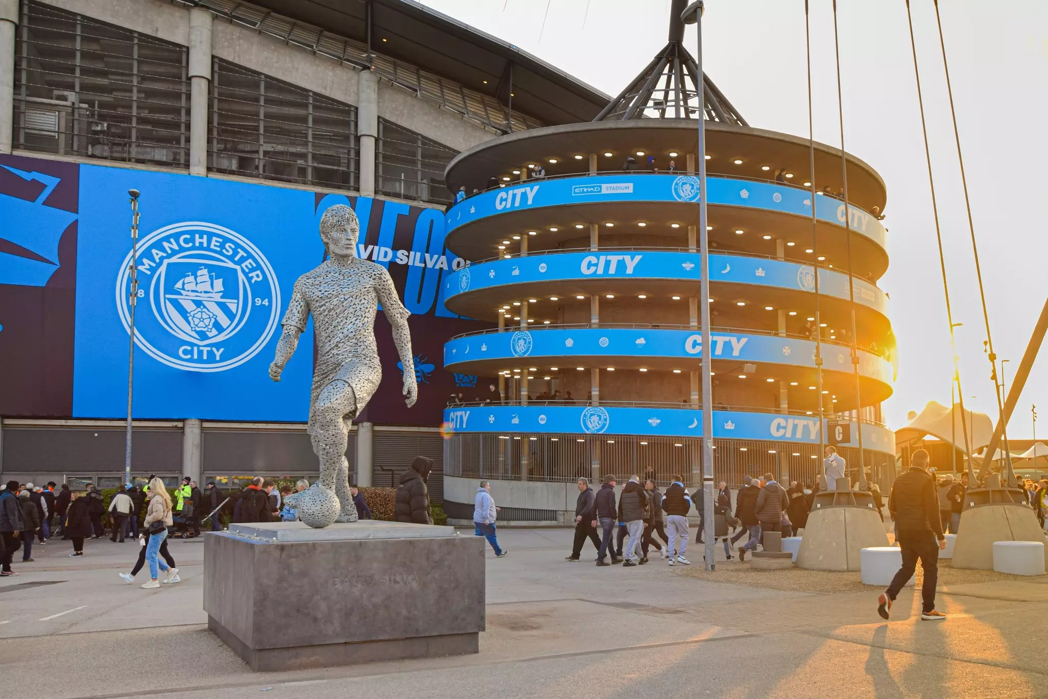 People pass by a stadium with a large statue of a footballer at the front