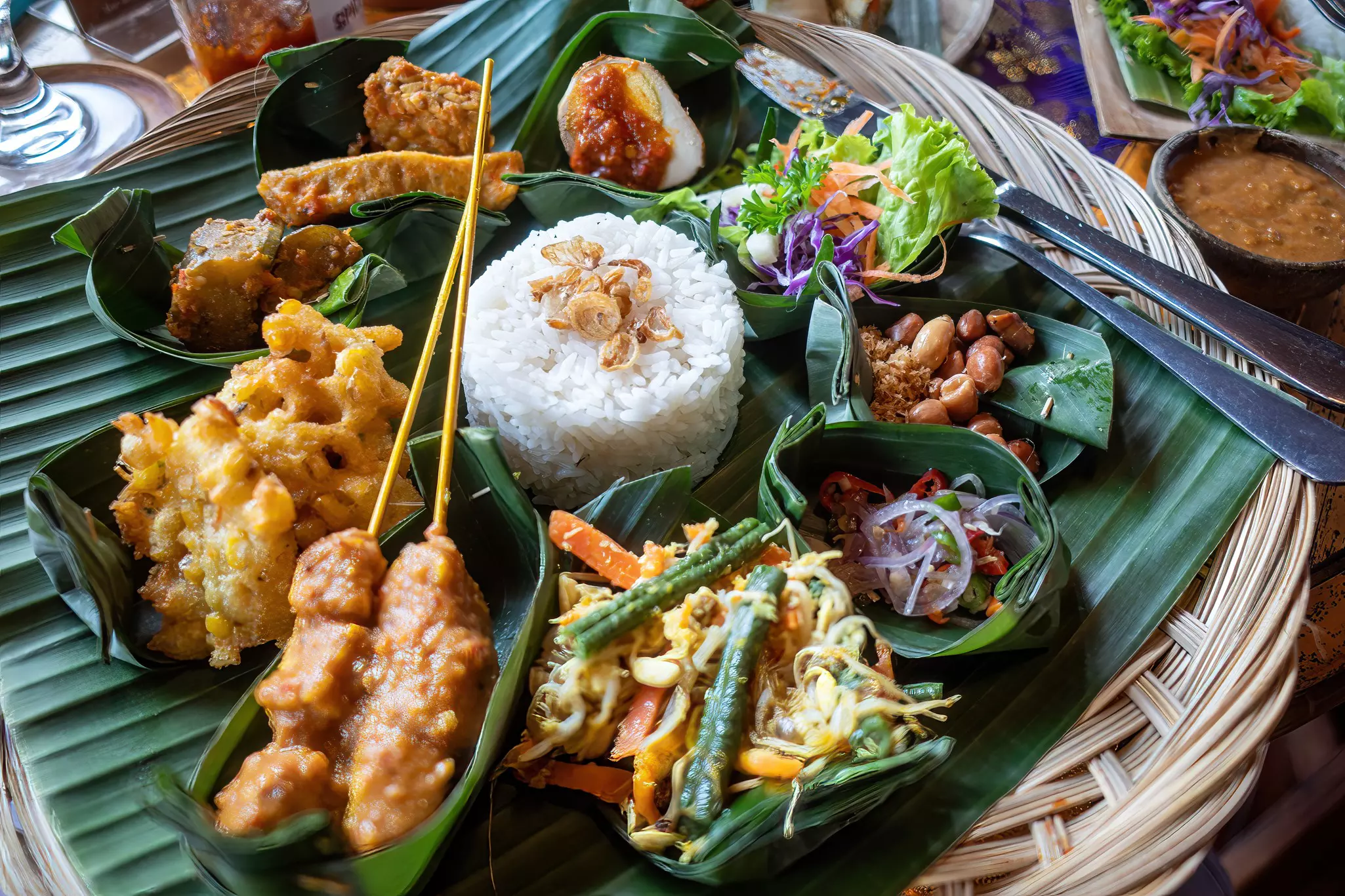 A plate of satay, rice, salad, buts and other Indonesian foods.