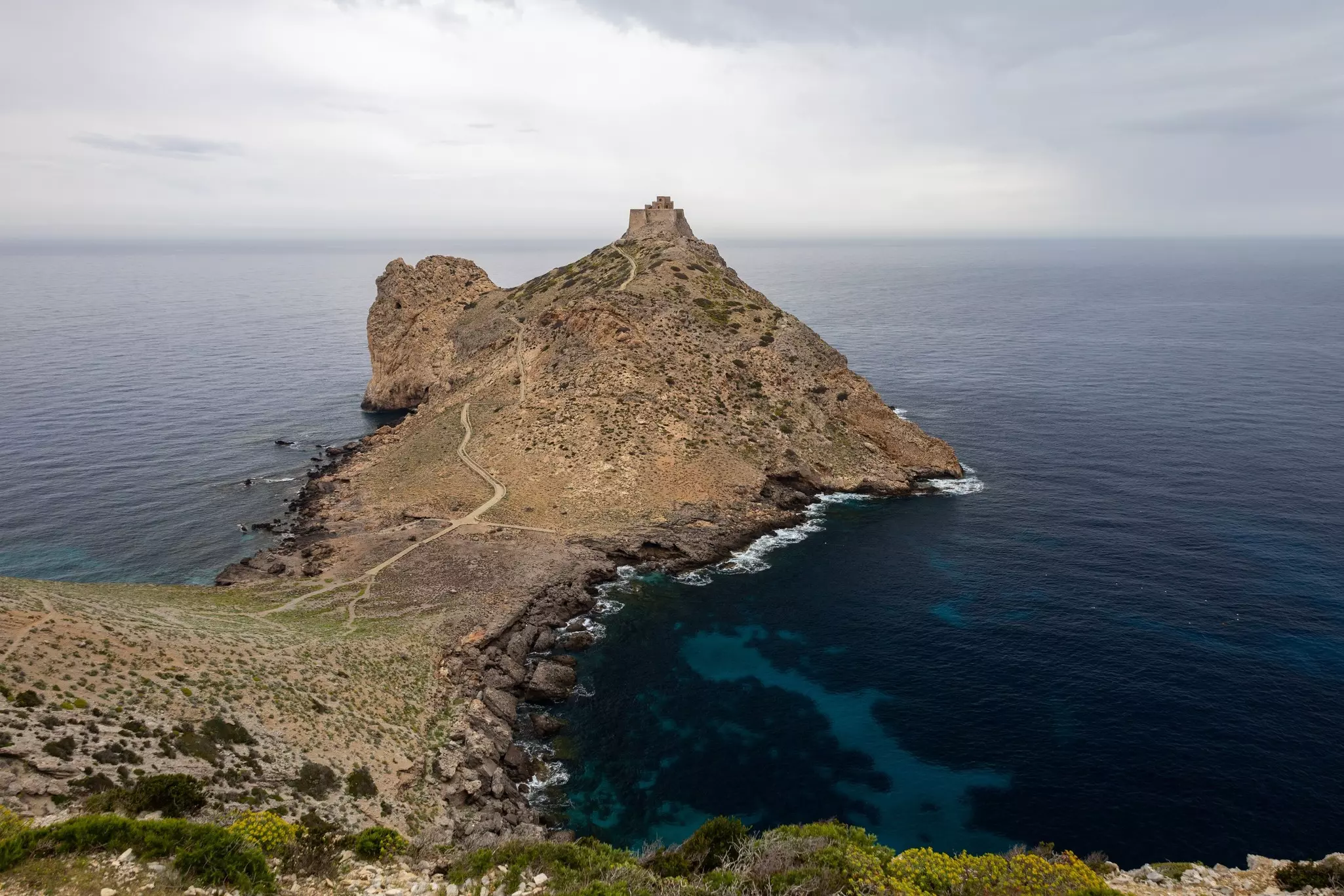 An old castle is seen at the top of a cape jutting into the sea.