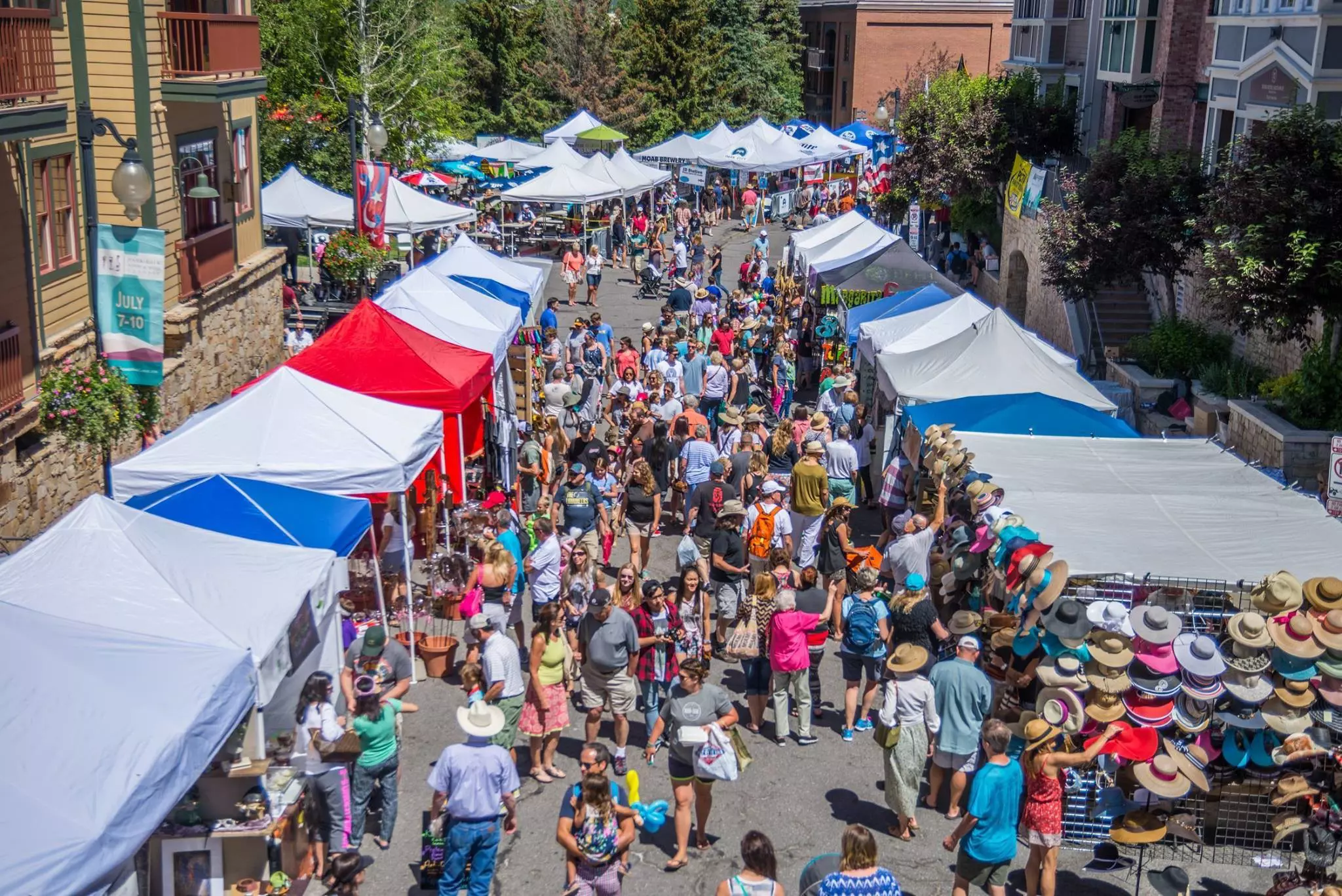 Aerial shot of people walking through busy market lined with tent-covered stalls on a sunny day.