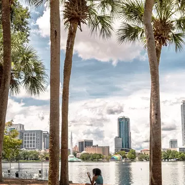 A girl sitting on grass overlooking water, surrounded by palm trees.