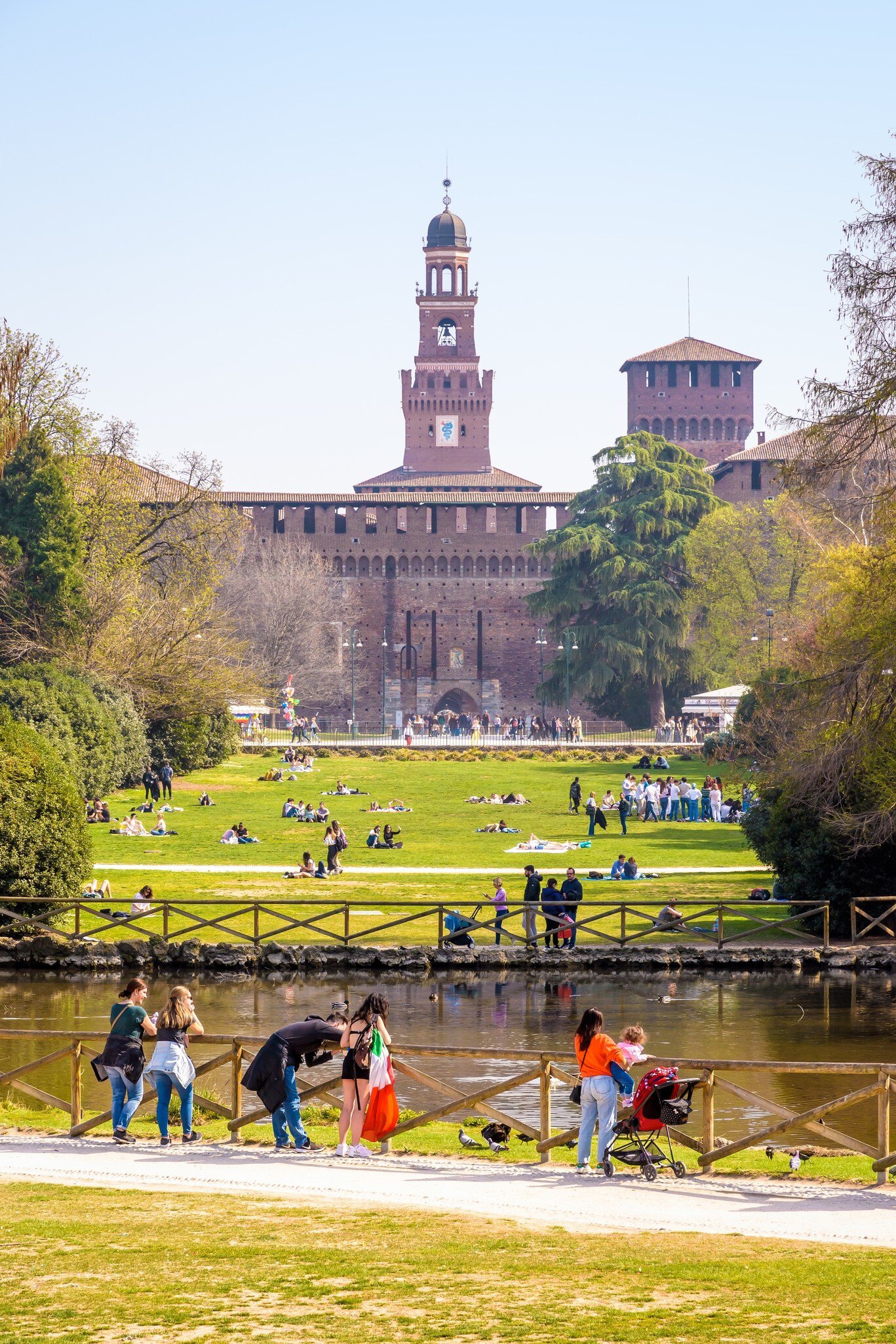 Milanese and tourists enjoy the Parco Sempione (Simplon park) overlooked by the towers of the Castello Sforzesco (Sforza Castle), on a sunny spring day.